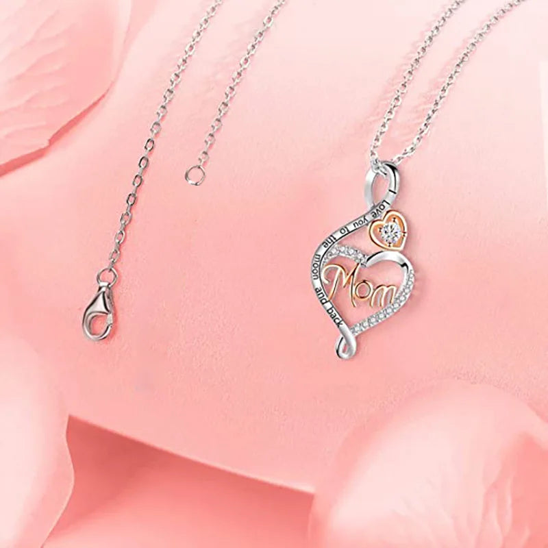 Silver heart-shaped pendant necklace with a gold accent and rhinestone details, displayed on a soft pink background.