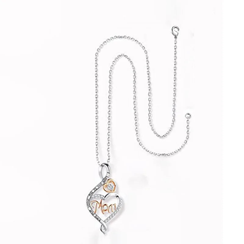A silver-toned necklace featuring a heart-shaped pendant with the word 'Mom' in cursive, accented by a small rose gold flower and clear rhinestones, displayed on a clean white background.