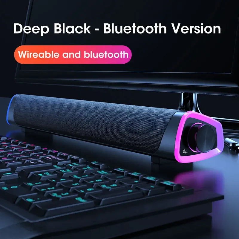 Gaming setup with a deep black Bluetooth speaker on a desk, keyboard, and monitor.