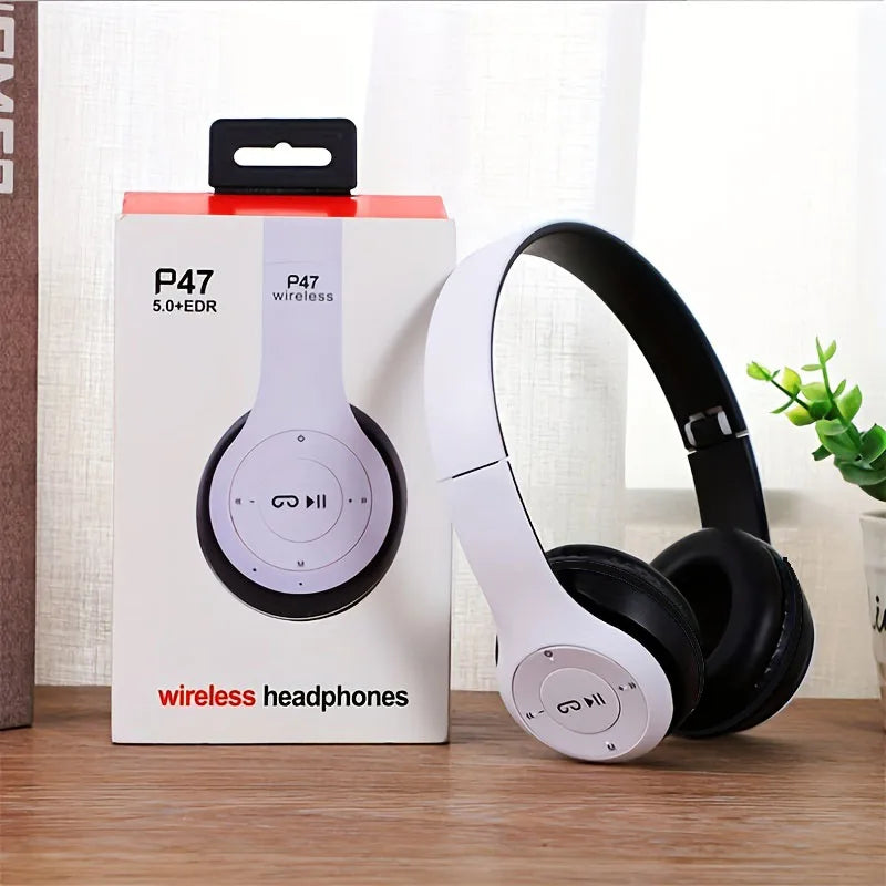 White and black wireless headphones next to their packaging on a wooden surface.