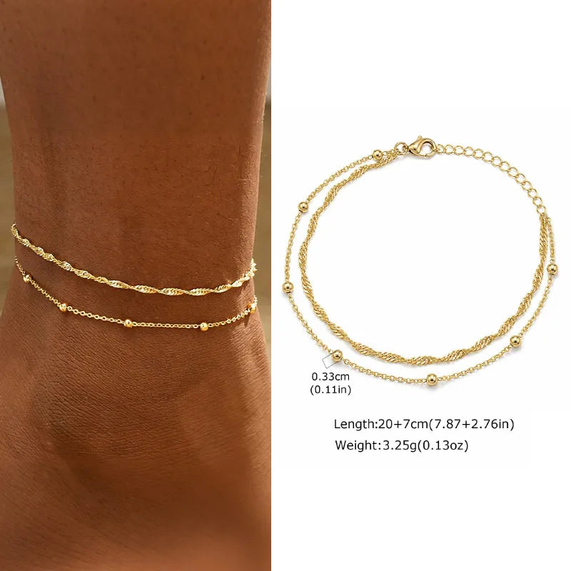 Gold anklets on a person's ankle with product details overlay.
