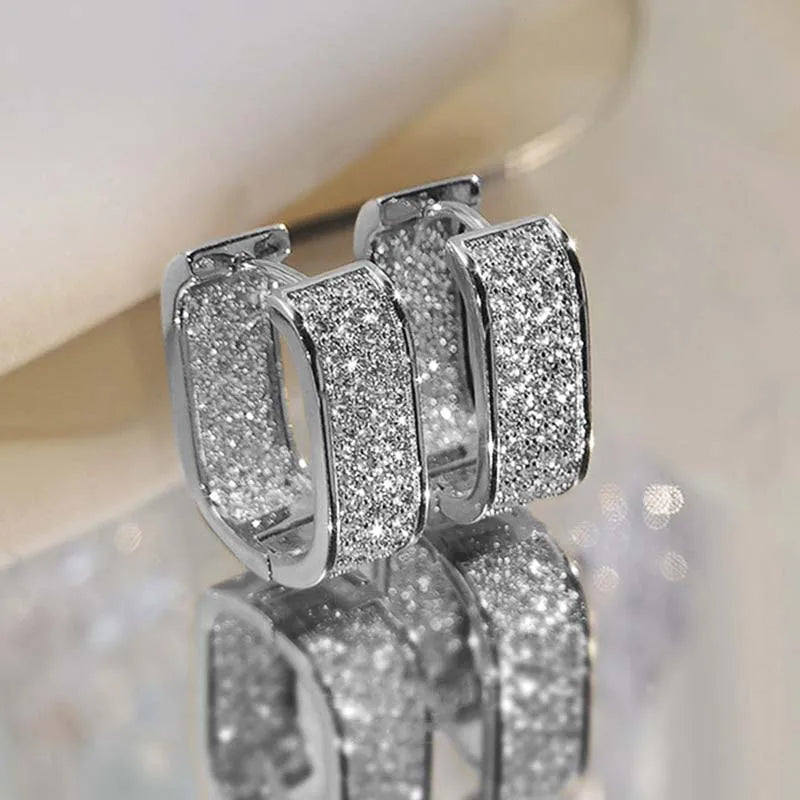 Silver hoop earrings with glittery finish on a reflective surface