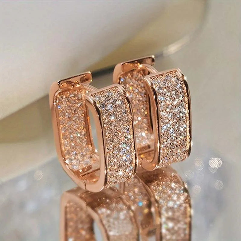 Rose gold hoop earrings with sparkling stones on a reflective surface.
