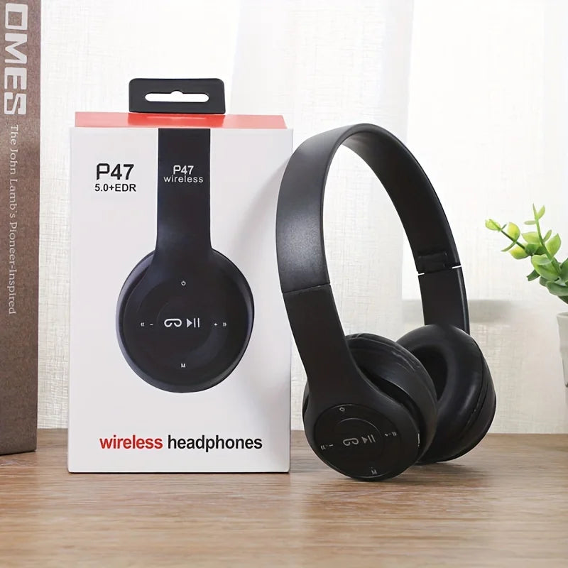 Black wireless headphones next to their packaging on a wooden surface with a white background