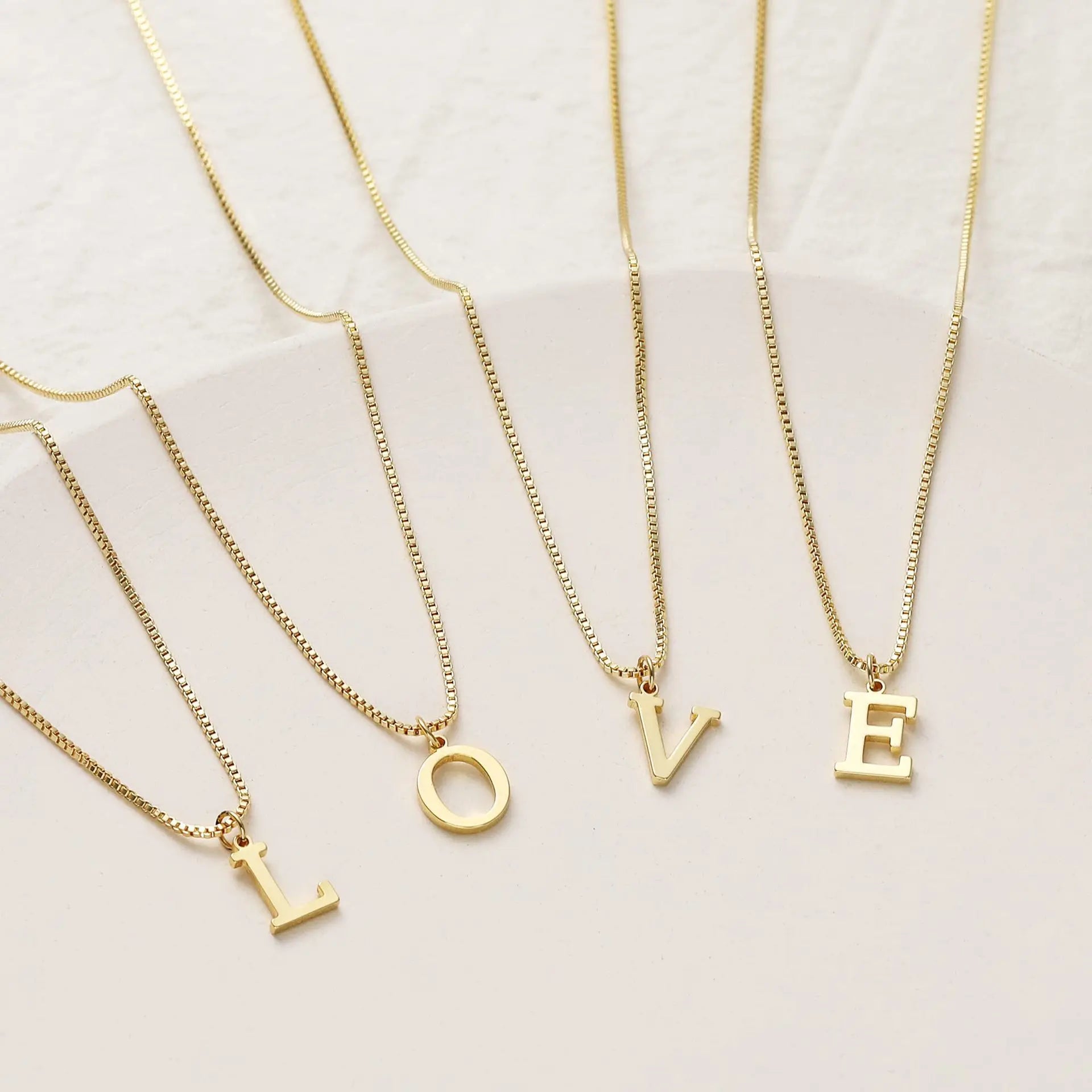 Gold necklaces with 'LOVE' letter pendants on a light background