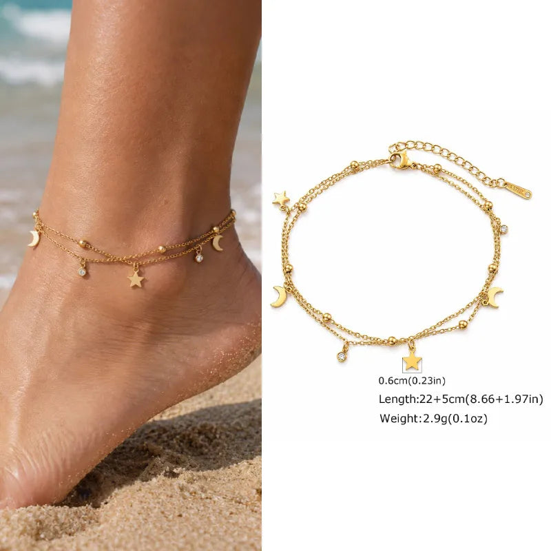 Gold anklets with star and moon charms on a beach setting
