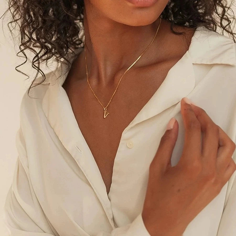 Woman wearing a gold necklace with a 'V' pendant, dressed in a white shirt.