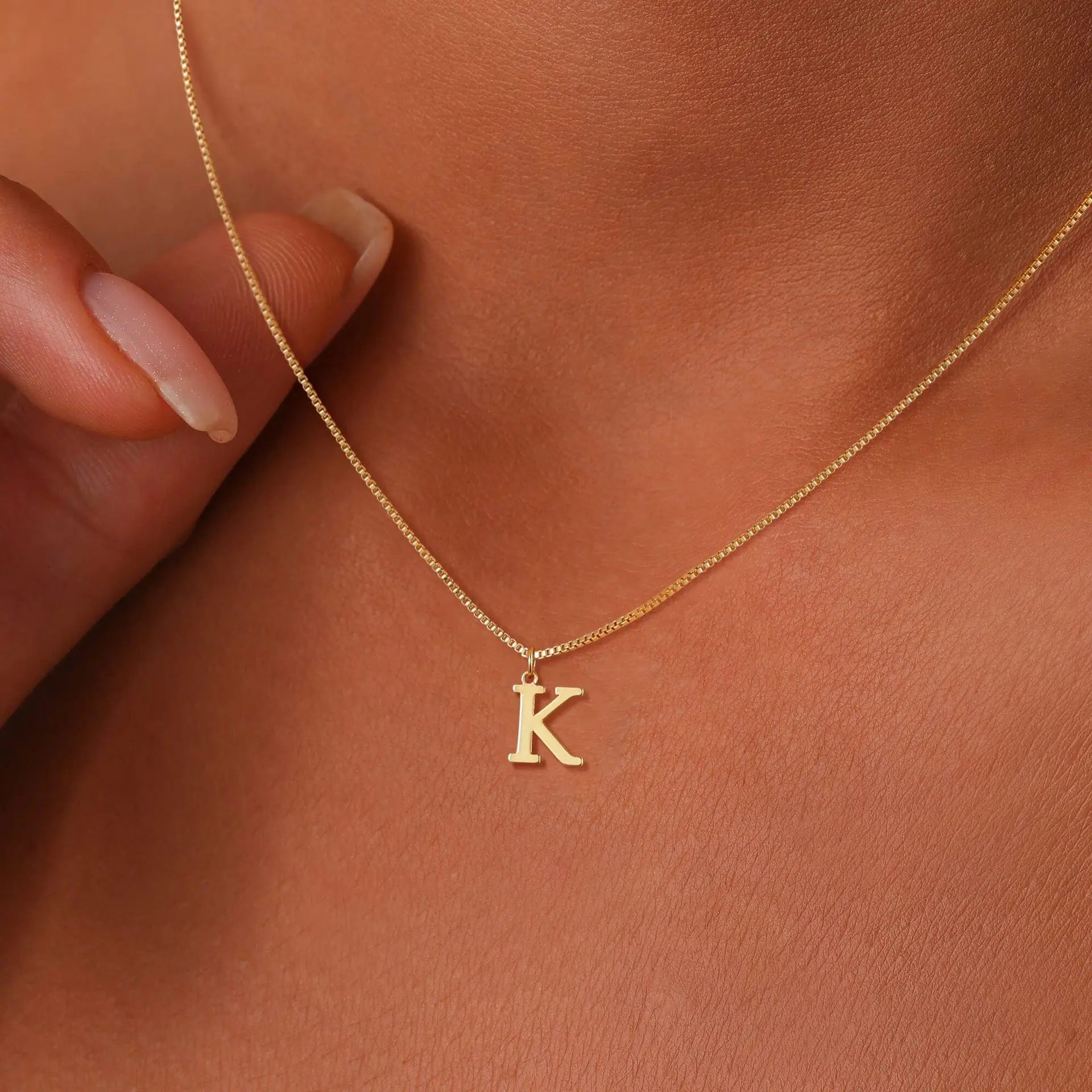 Gold necklace with a 'K' pendant on a person's neck against a brown background