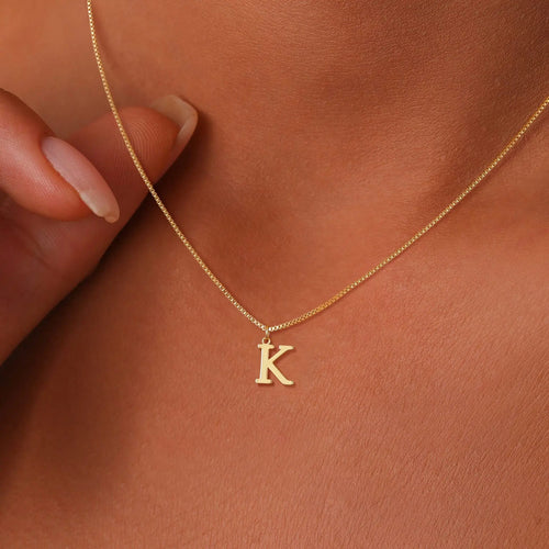 Gold necklace with a 'K' pendant on a person's neck against a brown background
