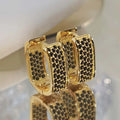 Gold hoop earrings with black gemstones on a reflective surface, brand 'ETERNITY' visible.