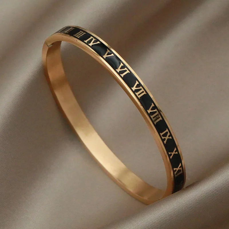 Gold bracelet with Roman numeral engraving on a beige fabric background