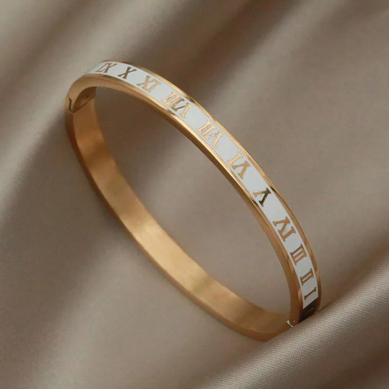 Gold bracelet with Roman numeral engraving on a beige fabric background
