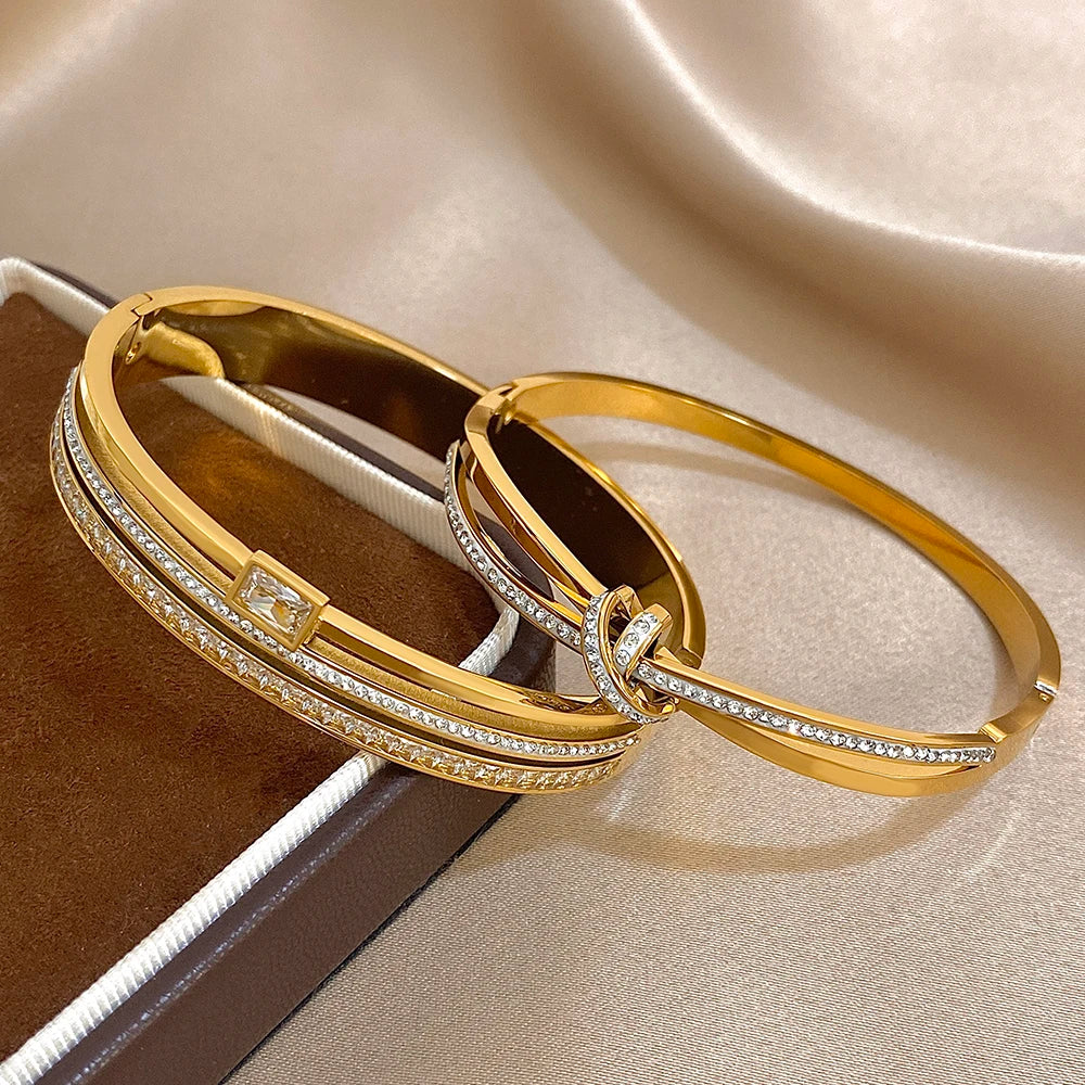 Two gold bangles with diamond accents on a beige fabric background